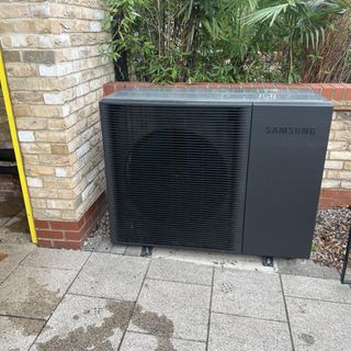 Samsung heat pump on patio near a brick wall