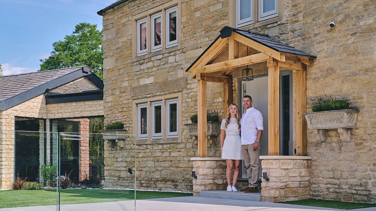 Young couple standing under a wooden porch outside their stone front home