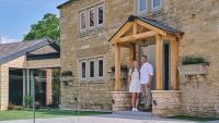 Young couple standing under a wooden porch outside their stone front home