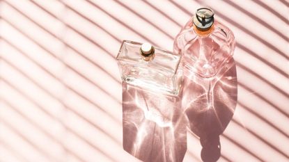 Two glass perfume bottles against a pink background to represent the art of fragrance layering