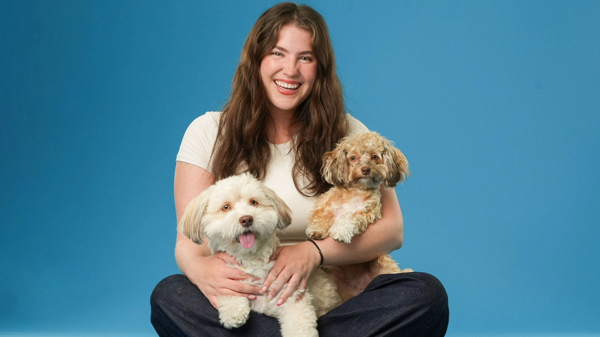 Gigi Robinson sat cross legged with her two dogs on her lap and a blue background behind them
