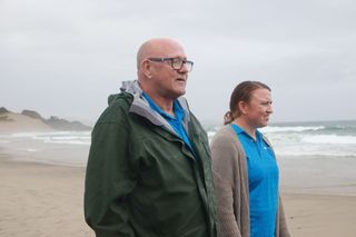 a man and woman walking on a beach with grey sky above