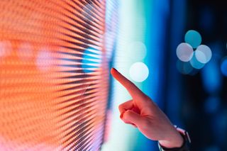 Close-up of female finger pointing LED display screen.