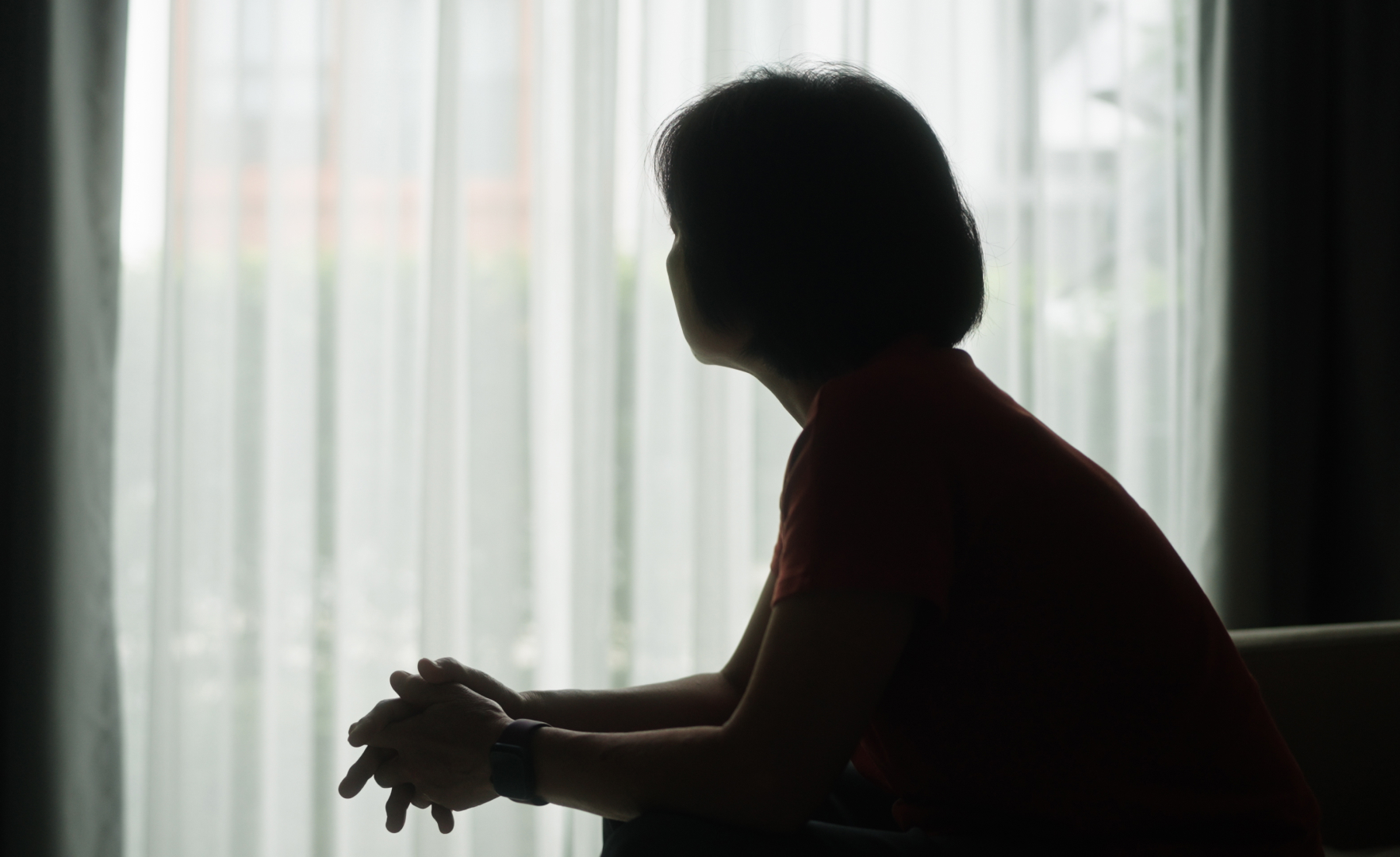 A silhouette of a woman sitting down and looking toward a window.
