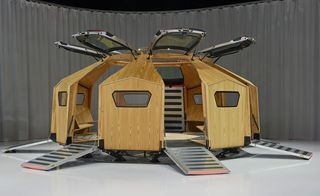 A futuristic mobile pavillion in oak colour with 7 entrances with the doors open (lifted up) with geometric shaped windows and metal platforms for each entrance.