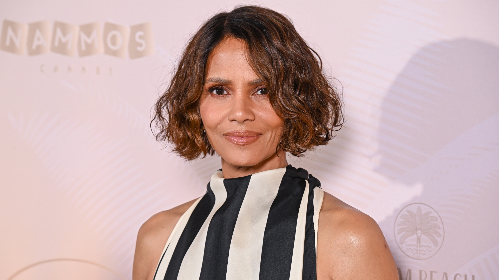 Image of Halle Berry smiling with curly brunette bob and wearing a vertical black and white striped halterneck gown