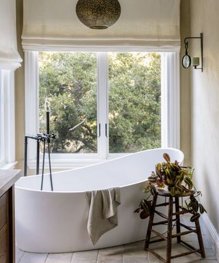 Neutral bathroom with a curved freestanding bath, a large window and a Moroccan metal pendant lamp