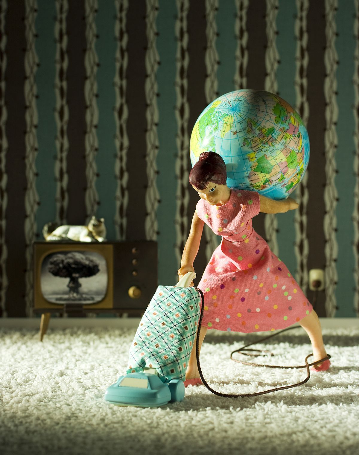 A doll (woman) in a pink polka dot dress balances a globe on her shoulder while vacuuming the carpet in a retro-themed living room