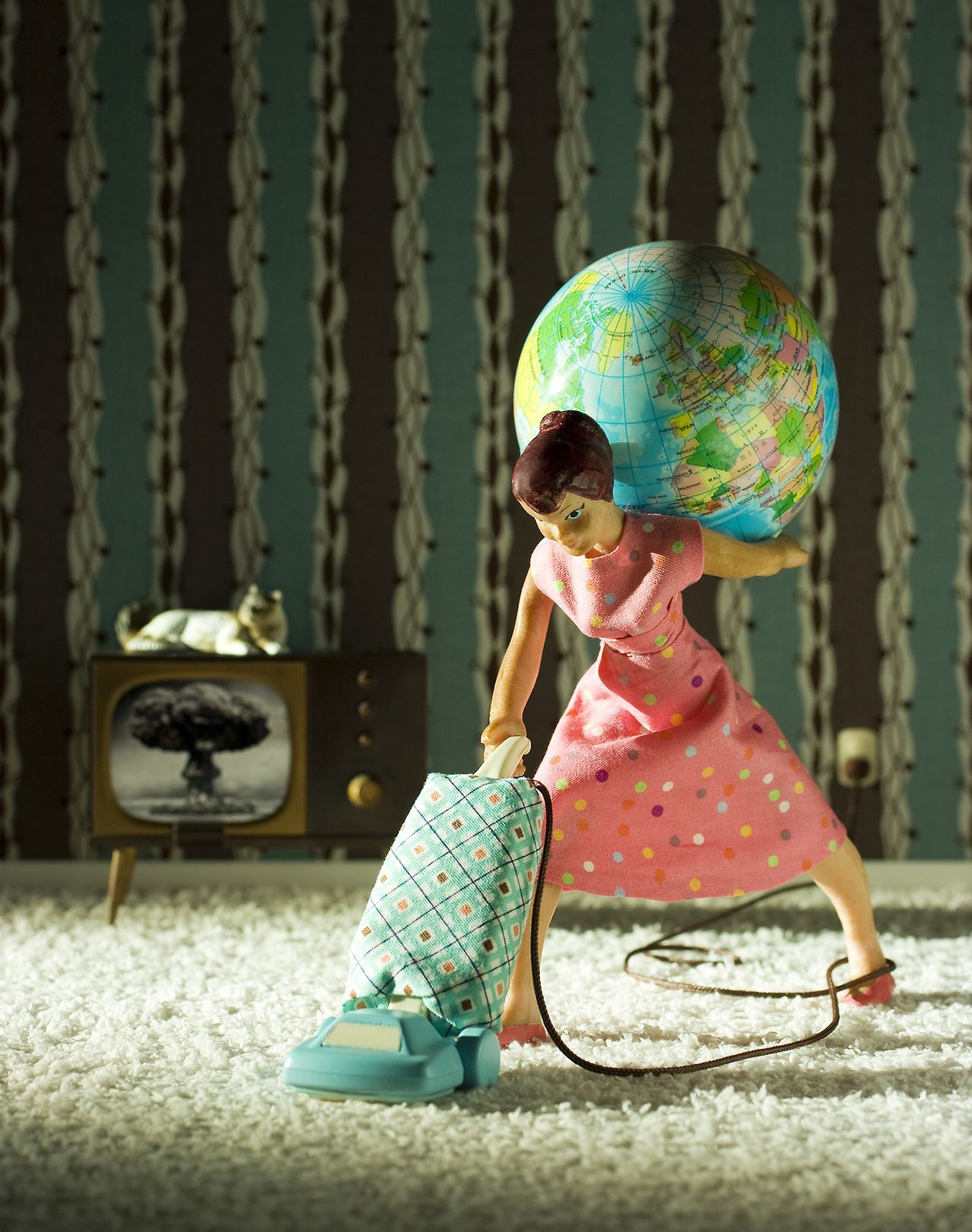 A doll (woman) in a pink polka dot dress balances a globe on her shoulder while vacuuming the carpet in a retro-themed living room
