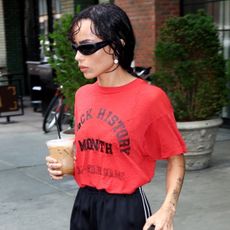 Zoë Kravitz in New York City wearing a red T-shirt that says "Black History Month" on it in red letters with black athletic shorts and peep-toe heeled sandals by Manolo Blahnik.