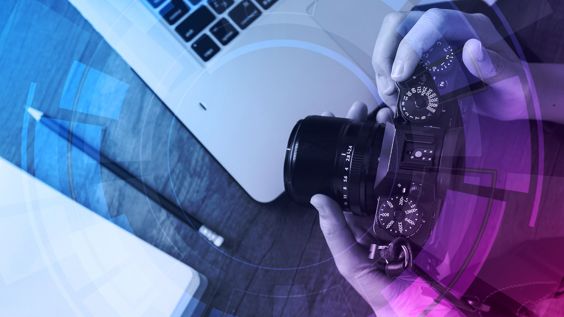 Two hands holding a camera above a laptop on a desk