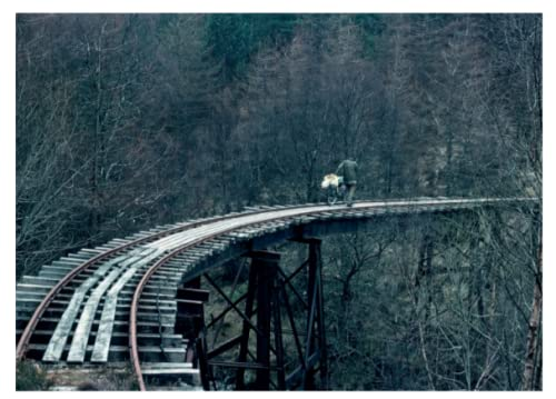 A cyclist pushes a bike across a railway bridge