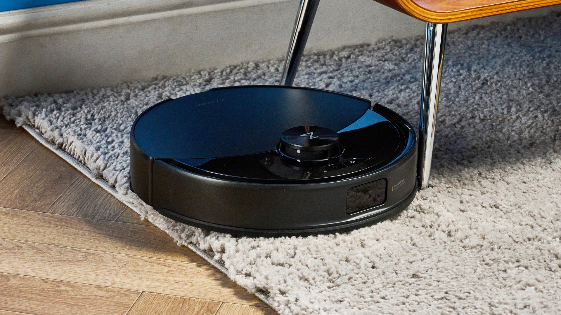 Roborock Q10 S5+ photographed on a wooden floor in front of a blue background
