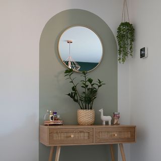 green painted arch behind wood console table round mirror hanging planter