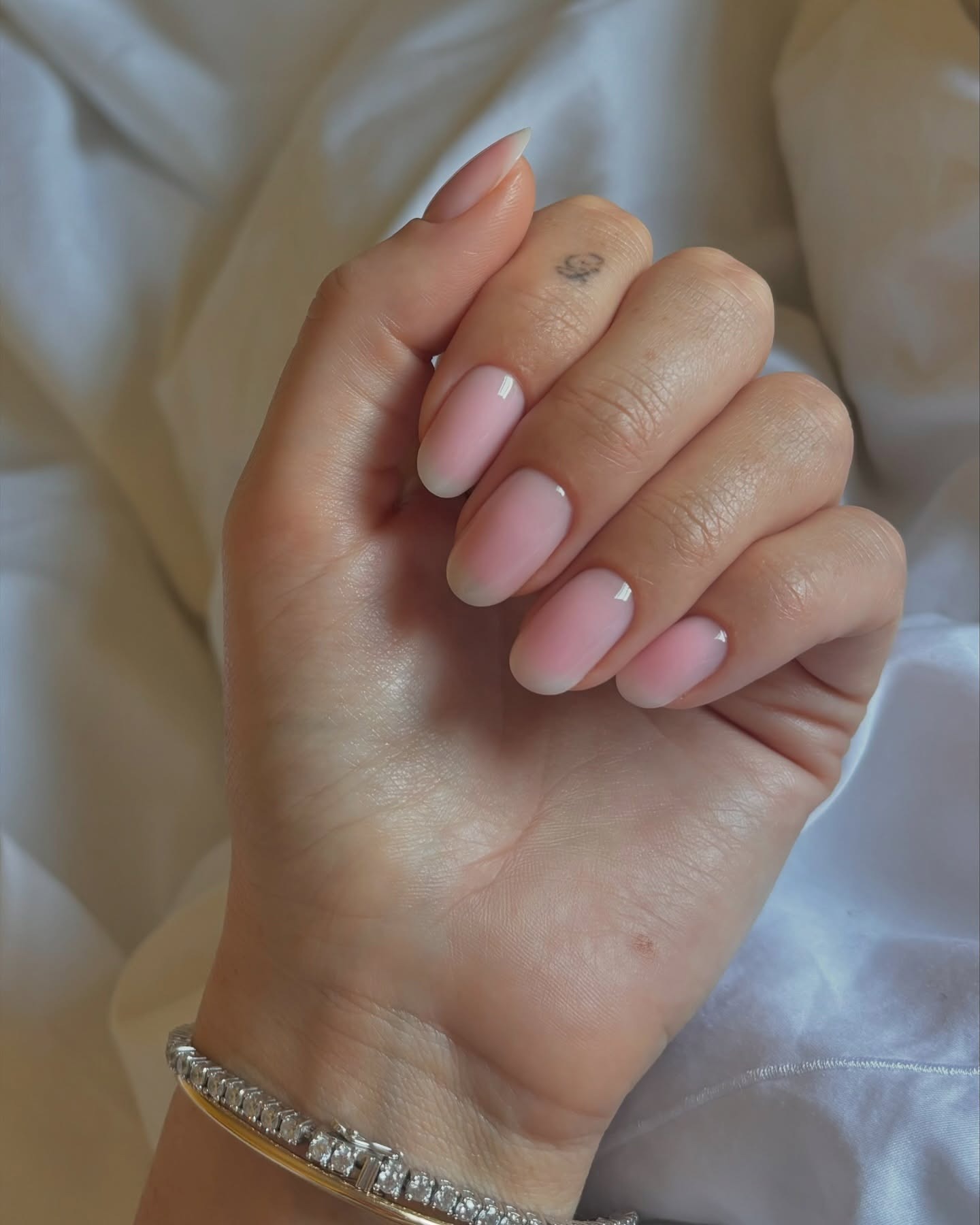 A woman's hand on a white bed sheet with a blurred French manicure nail design