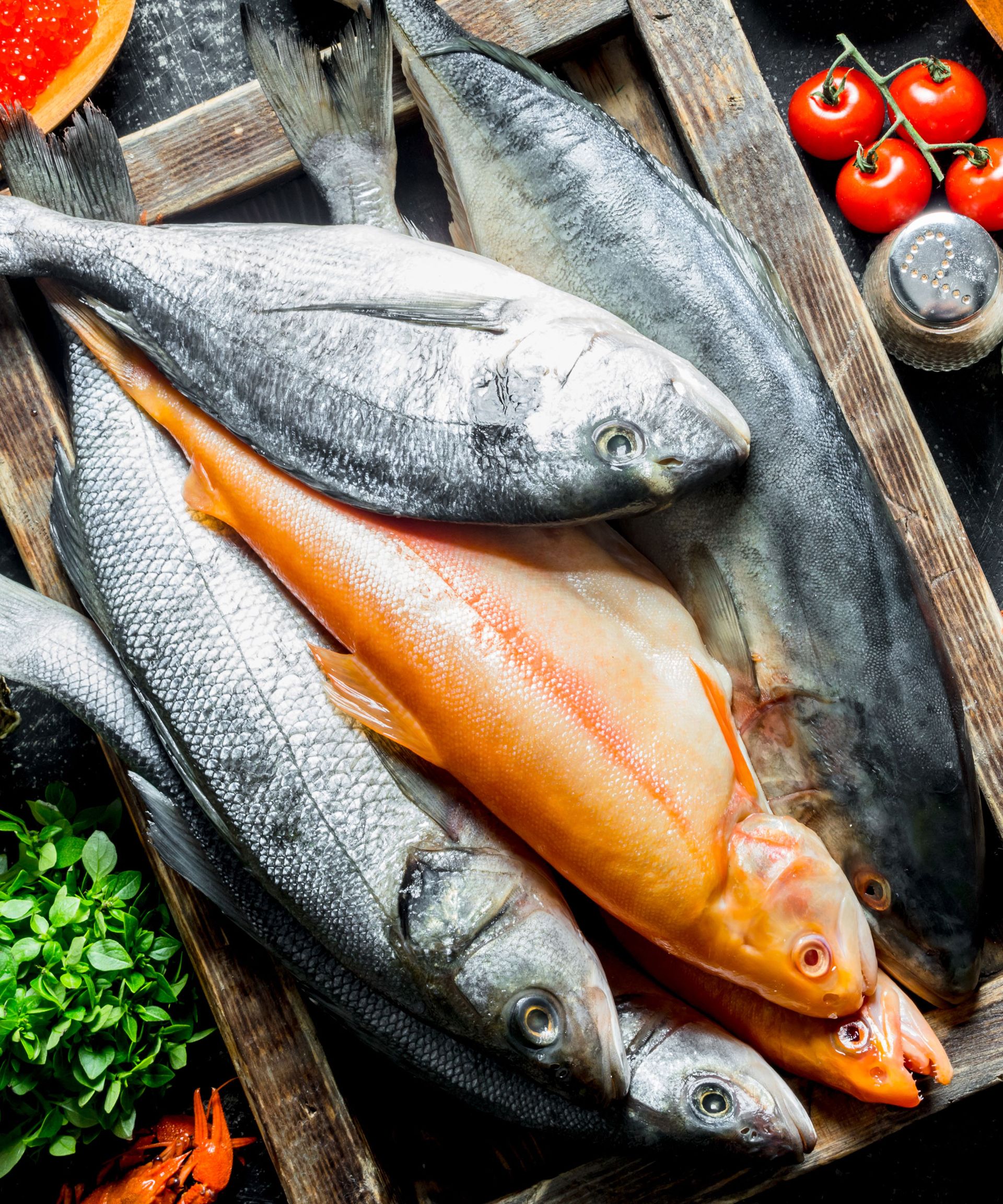 large fish sitting on wooden board with tomatoes and parsley