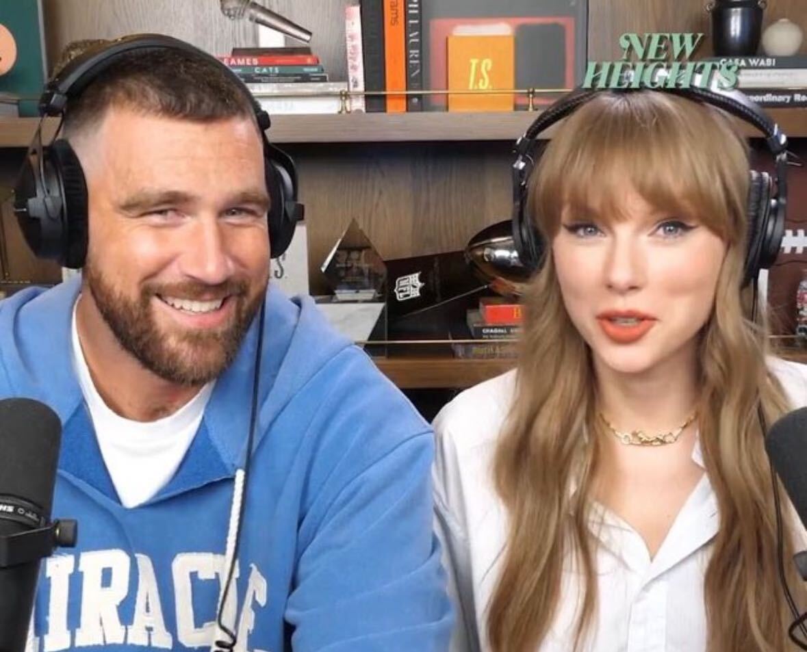 Taylor Swift and Travis Kelce sit in his home podcast studio where Swift wears a white shirt and Cartier necklace