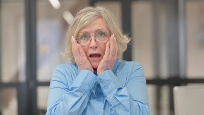 An older woman puts her hands on her cheeks with a look of surprise.