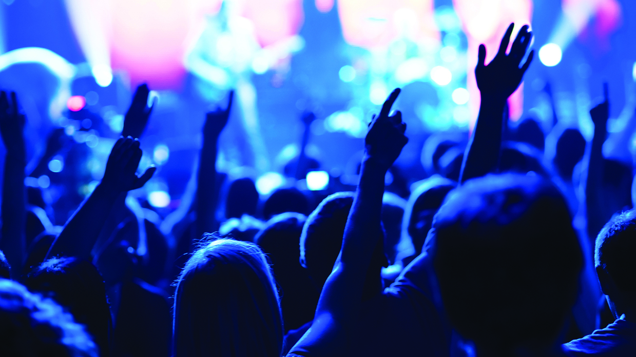 A crowd at a concert with their arms raised in the air.