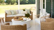 back porch patio with dark green slatted doors, white floor, wicker furniture and tub chairs styled for fall