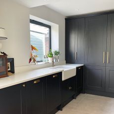 Charcoal grey kitchen with white worktops, a butler sink and a floor to ceiling bank of units