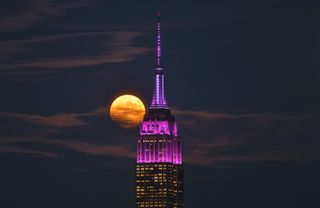 full moon shining bright behind the empire state building lit up in purple lights