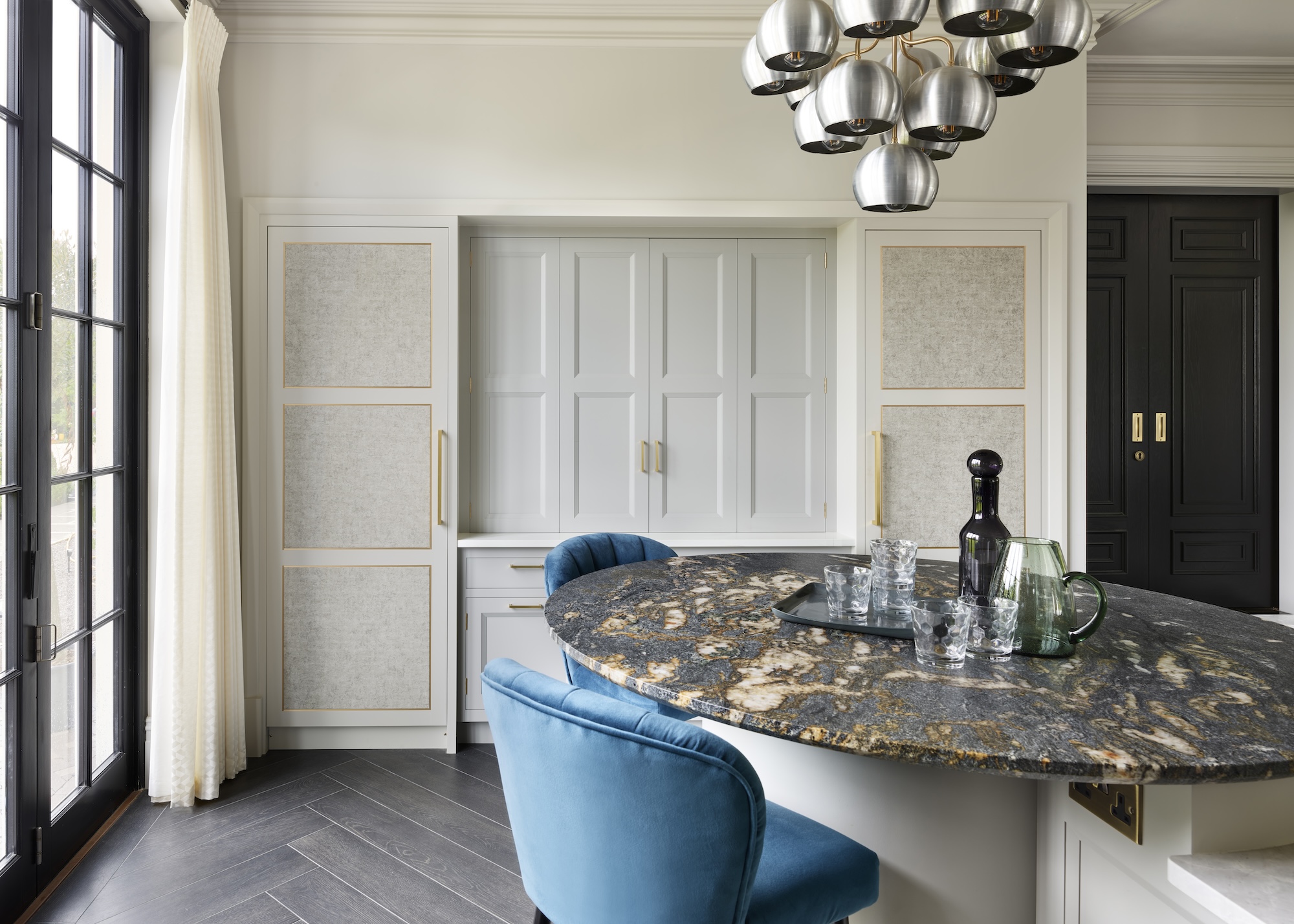 A kitchen with a large dining table with a marble top, pendant lights hanging above and light blue chairs beside the table.