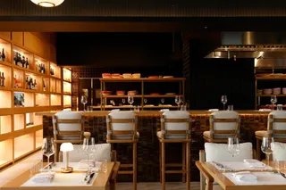 The intimate dining area of an Italian-inspired restaurant features tall white upholstered wooden stools, mushroom-shaped lamps, and wine glasses.