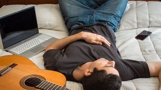 Young man using smart phone while sitting at home with guitar in background