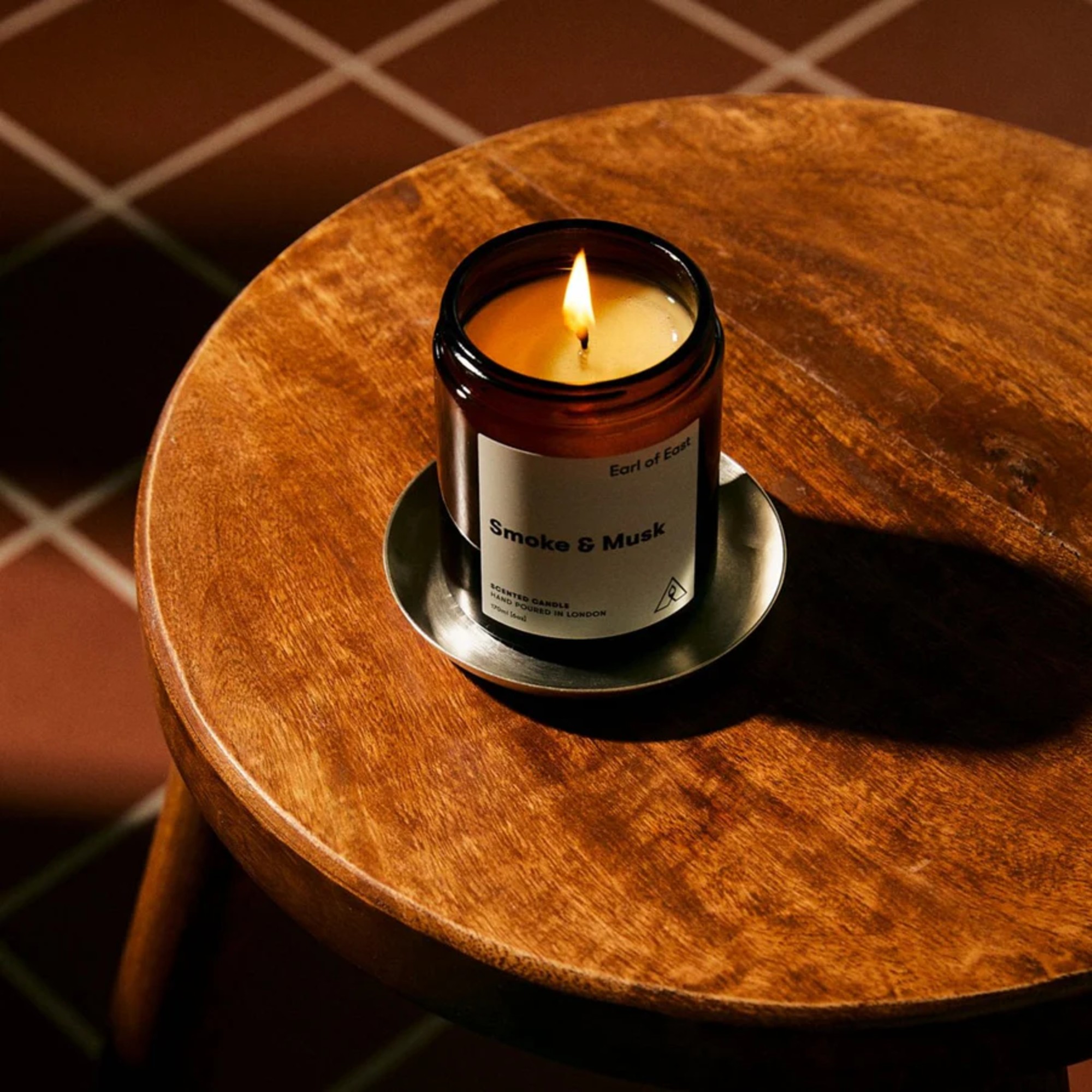 A lit Smoke &amp;amp; Musk scented candle from Earl of East on a wooden side table