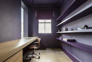 closet office with aubergine/eggplant walls and shelving, blind, wooden floor, wooden desk, leather and chrome chair
