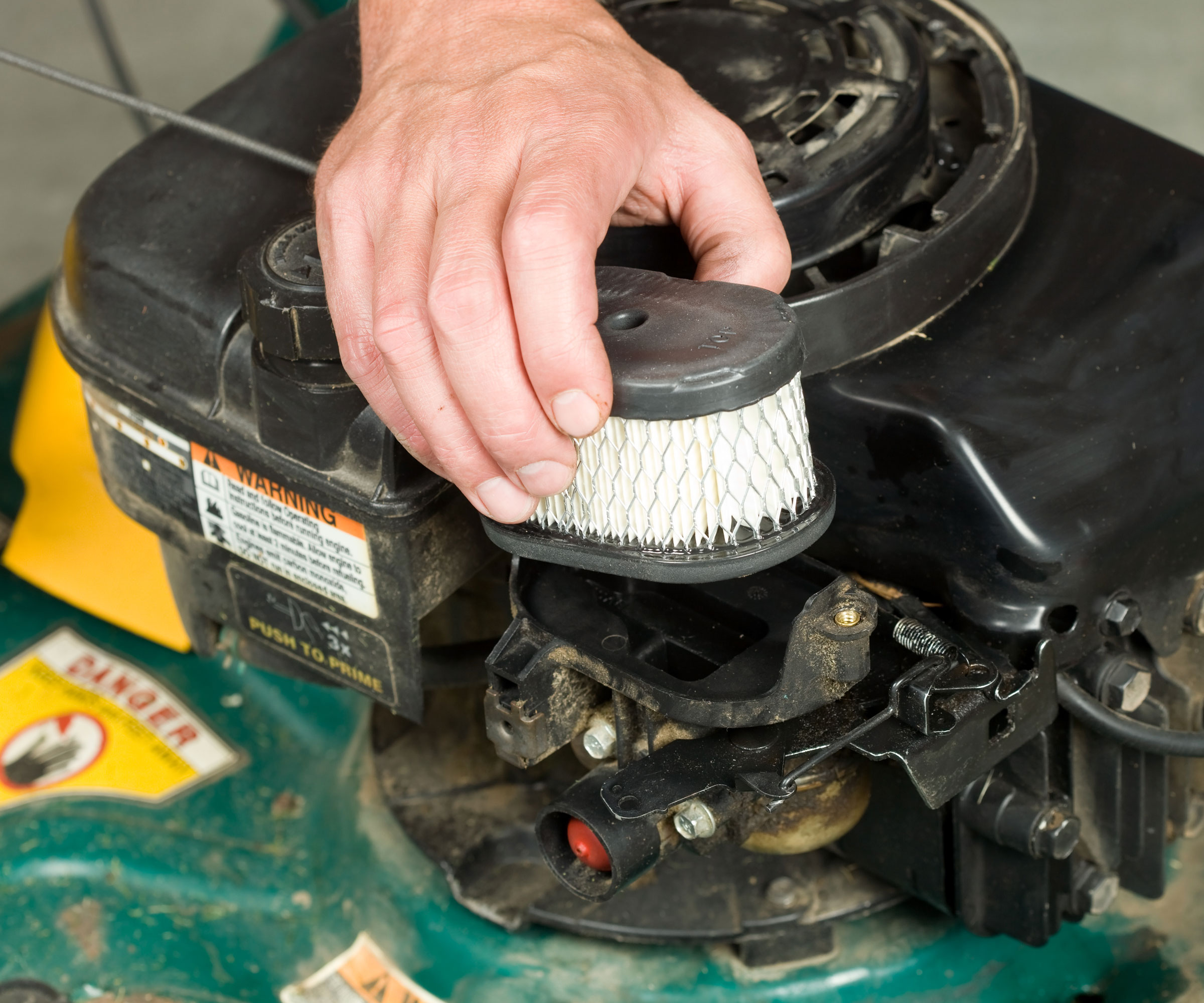 hand holding air filter in front of lawn mower engine