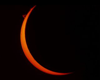 a large portion of the sun is covered by the moon, leaving a thin orange crescent which almost looks like a crescent moon in the night sky.