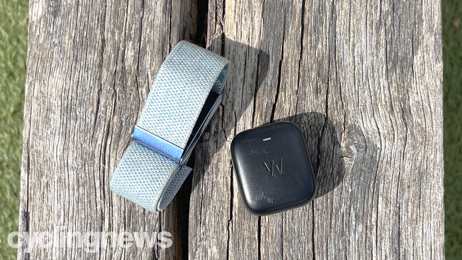 A close up of the Whoop 4.0 wrist strap heart rate monitor on a wooden bench. The strap itself is a light blue colour, and sitting next to it is the charger, which can be clipped on to charge it while wearing