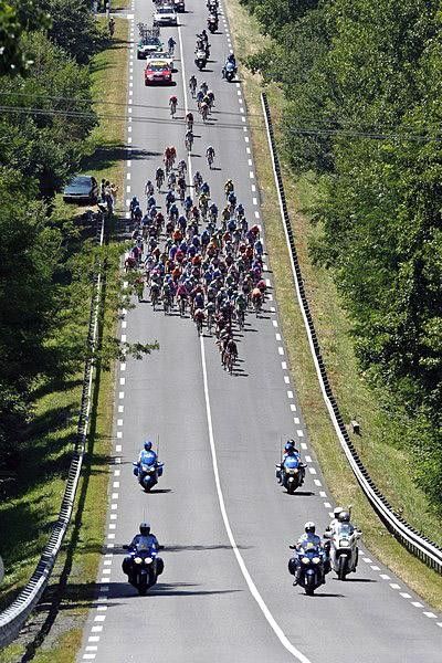 The peloton streams down a long straight road.