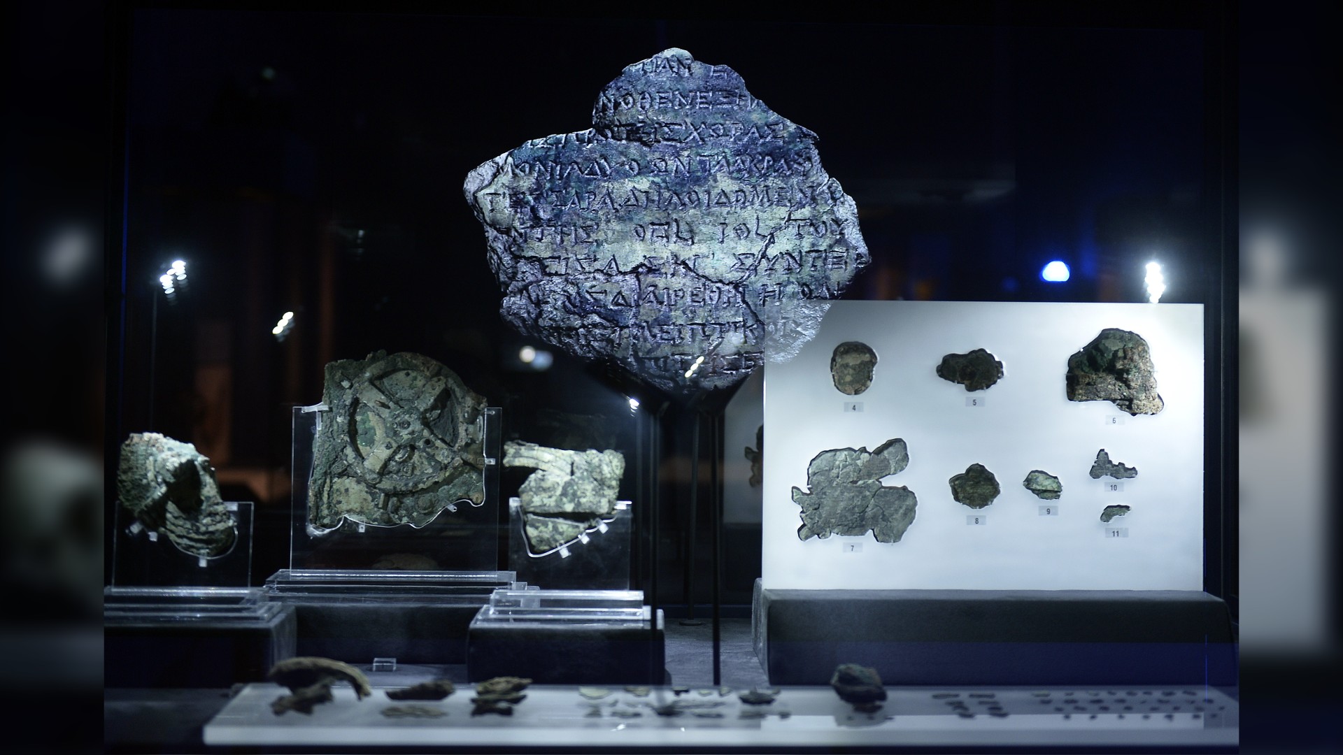 A picture taken at the Archaeological Museum in Athens on September 14, 2014 that shows pieces of the Antikythera Mechanism, a 2nd-century B.C. device known as the world's oldest computer which tracked astronomical phenomena and the cycles of the Solar System. Here we see several items on display, all quite eroded. In the center there is a large piece that has some writing on it in an old language.
