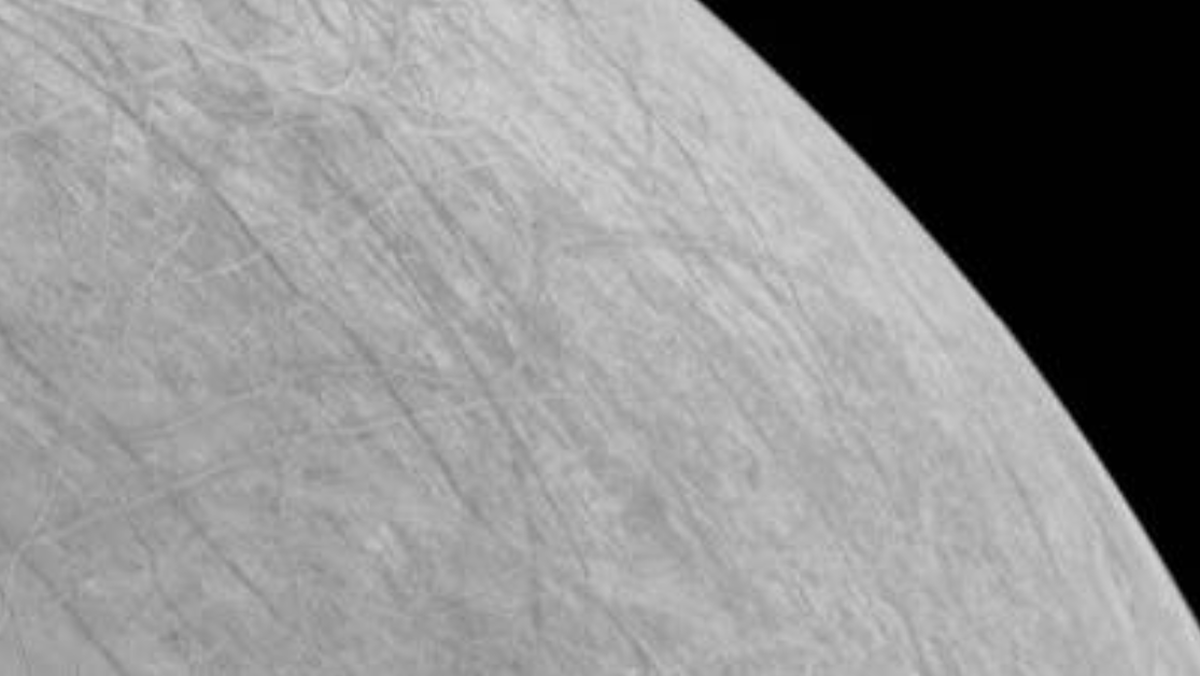 black and white view of criss cross of icy streaks on jupiter&#039;s europa with black sky in behind