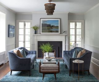 Living room with large blue area rug beneath central coffee table, between two 3-seater blue upholstered couches with a cozy, classic fireplace
