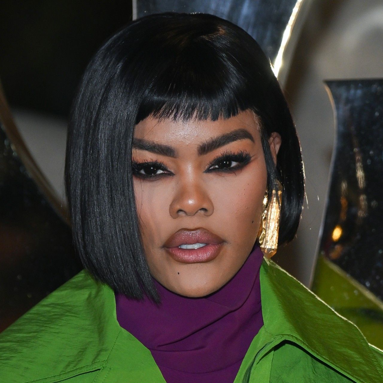 a black woman wears a black bob haircut and dark eye makeup while posing for paparazzi at an event