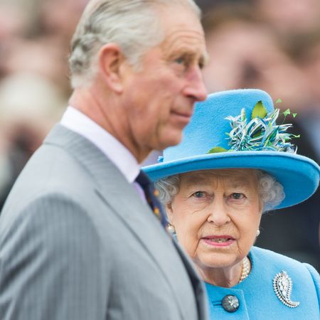 King Charles is in side profile and has white gray hair while wearing a gray pinstripe suit while his mother, Queen Elizabeth II, wears a turquoise blue coat dress and matching hat
