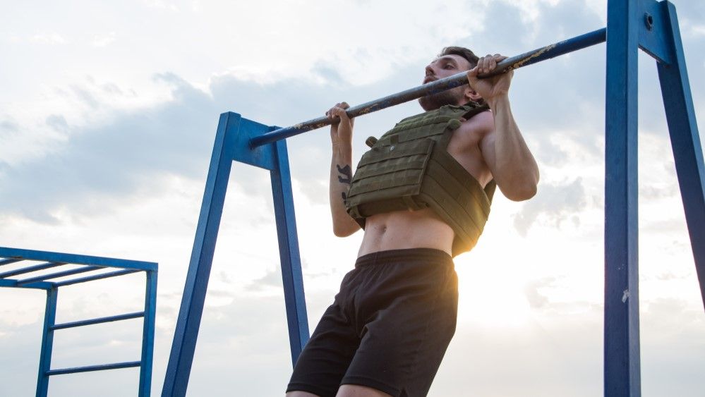 a photo of a man doing a pull-up in a weighted vest 