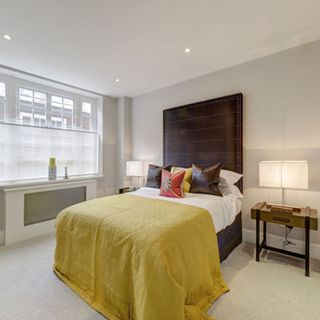 bedroom with white wall brown bed with coloured cushion white window and wooden flooring