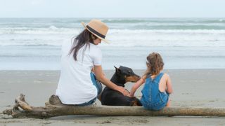 Doberman sitting with mum and daughter on the beach