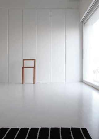 White room, with a white and black striped rug and a small wooden stool