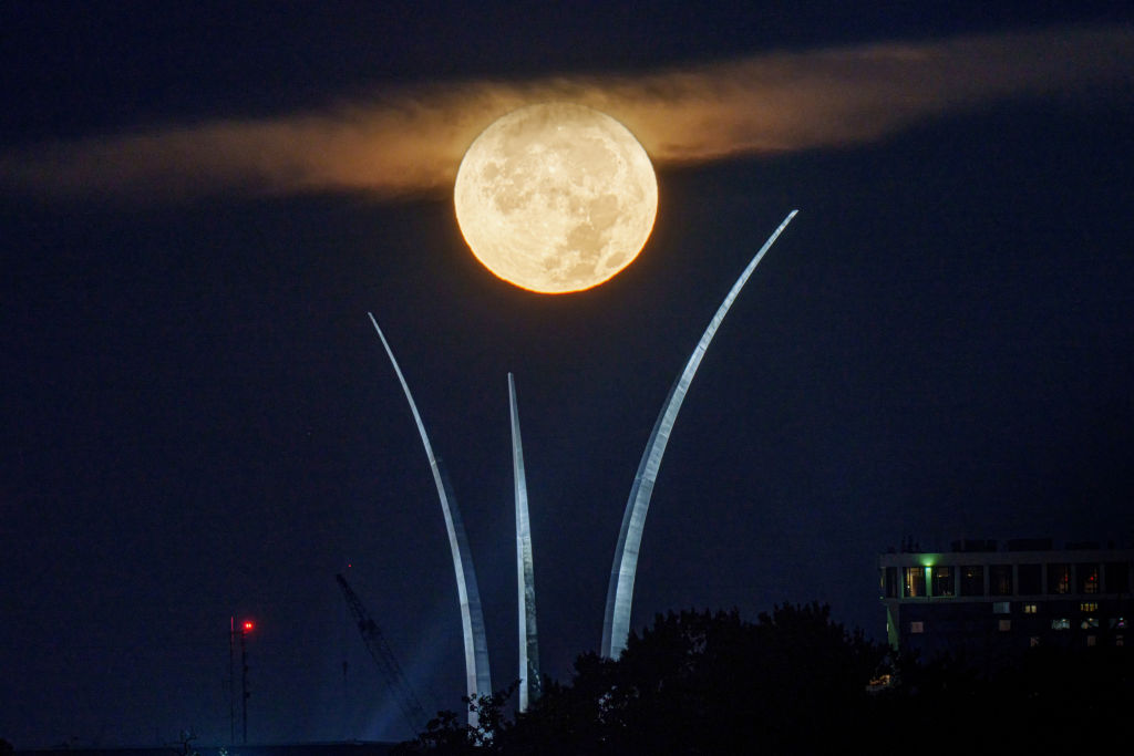 Una luna llena brillante detrás de una nube sobre tres grandes torres que se elevan hacia el cielo.