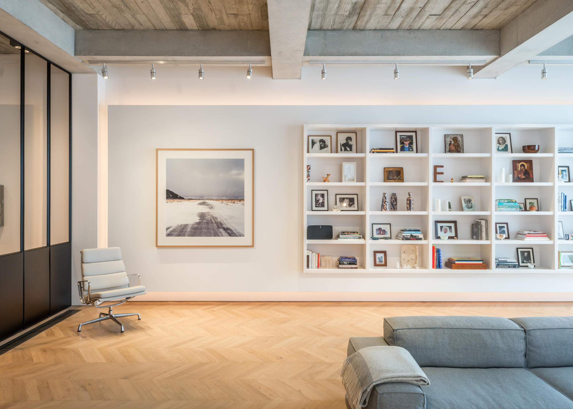 white living room with gallery wall and a large open shelving unit with books and images on it. There is also a view of the sofa as well as a chair placed in the corner of the room