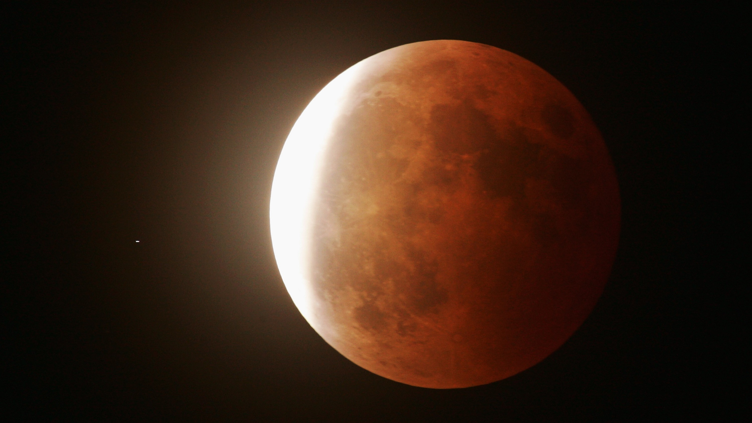 A partially eclipsed full moon is shown with its right side covered in Earth's shadow and a thin crescent illuminated in direct sunlight to the left.