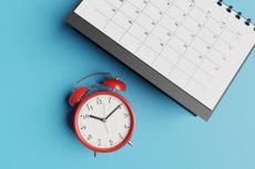 red analog clock placed next to a calendar with a teal blue backdrop