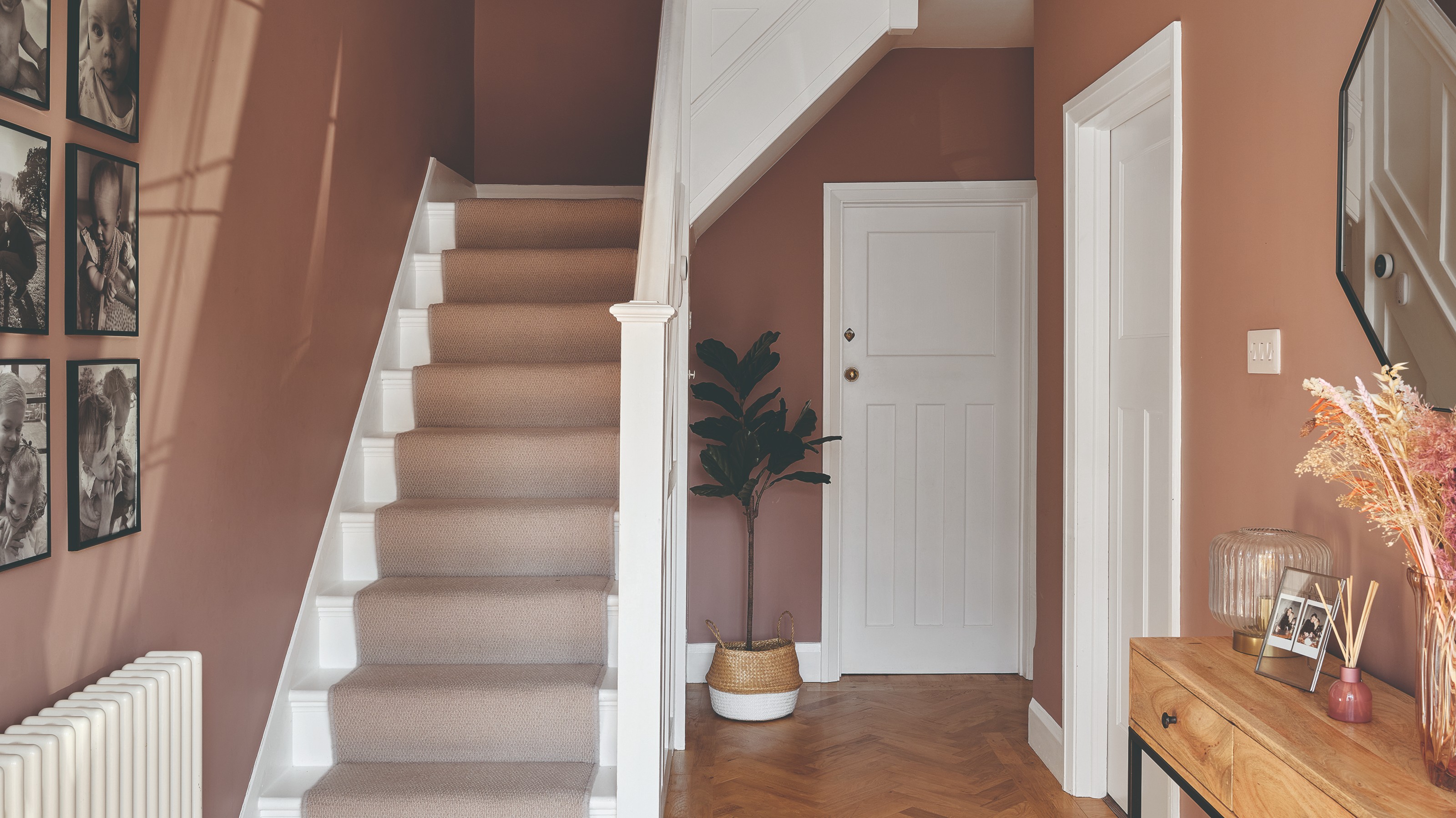 A soft brown-painted hallway with a white-painted staircase and a beige runner on top