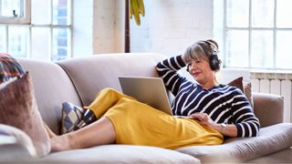 Woman sitting on sofa with laptop and headphones relaxing